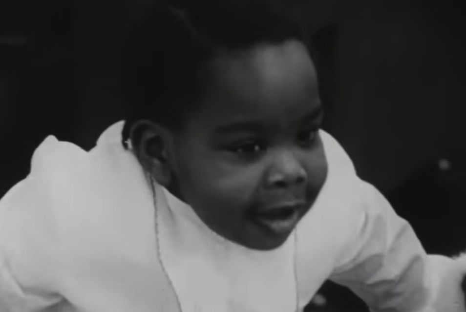 A baby looking toward the camera in a black-and-white still from Robin, Peter, and Darryl Three to the Hospital