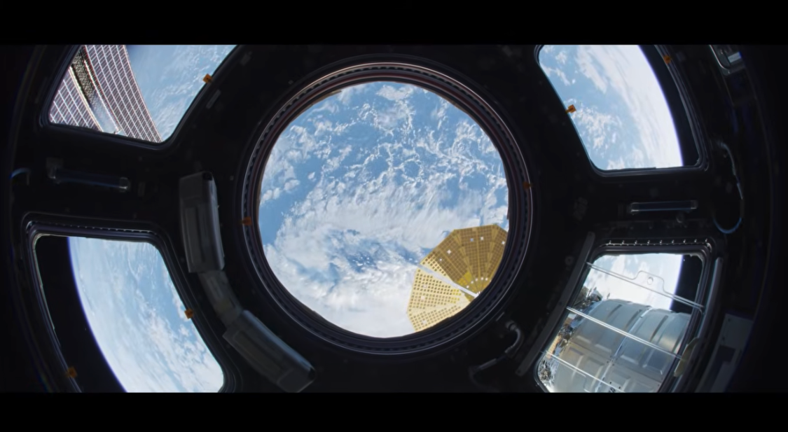 Earth seen through the seven windows of the International Space Station's Cupola observation module, with a solar array in view, in a still from International Space Station: Humanity's Lab in Space