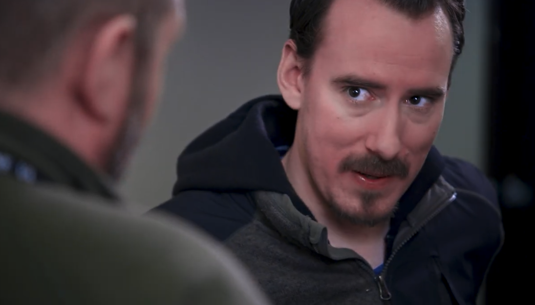 A young Marine veteran listening intently to an older veteran in a VA hallway in a still from My Whole Health Journey