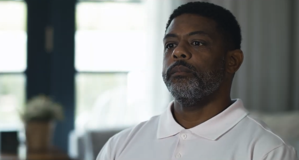 A father in a white polo shirt listening thoughtfully during an interview about his child's sickle cell diagnosis, in a still from A Sickle Cell Anemia Diagnosis