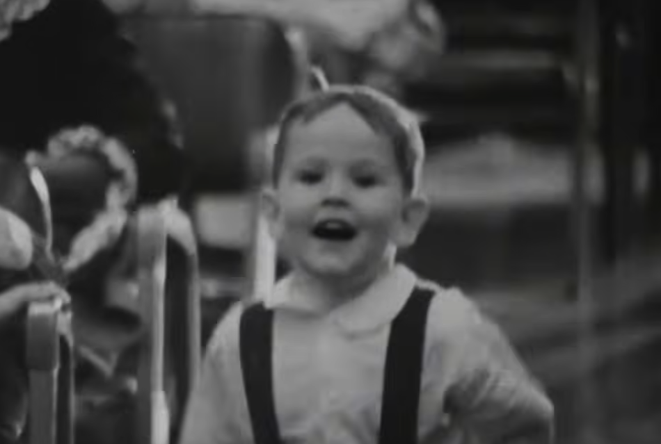 A young child smiling in a black-and-white still from Robin, Peter, and Darryl Three to the Hospital
